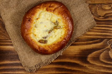 Sweet round bun with cottage cheese and raisins (cheesecake) on wooden table