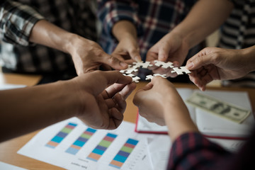 Hands group of business people assembling jigsaw puzzle white. Below is the graph paper business documents placed on a wooden table in the meeting room.