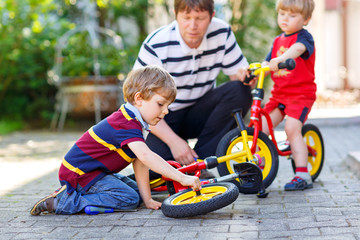 Two happy little kid boys and father repair chain on bikes and change wheel of balance bicycle