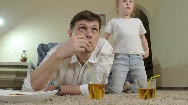 man and daughter watching television, sitting on the floor drink juice