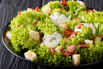 Organic French Lyonnaise salad with lettuce, bacon, croutons and poached eggs close-up on a plate on the table. horizontal