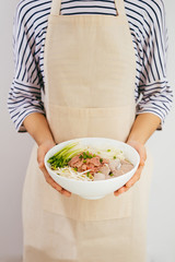 Female chef prepare traditional Vietnamese soup Pho bo with herbs, meat, rice noodles