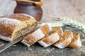 Naklejka premium A loaf of rye bread oval shape and cut slices on wooden Board vintage, rustic style, homemade cakes close-up,