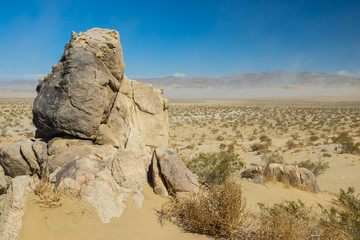 Fototapeta na wymiar Tall stone boulder stands above massive sand wilderness in the desert of southern California.