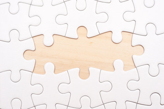 White blank puzzle with 2 pieces missing on wooden board with copy space.