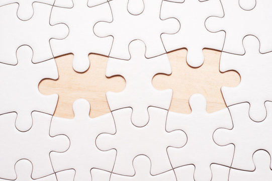 White blank puzzle with 2 pieces missing on wooden board with copy space.