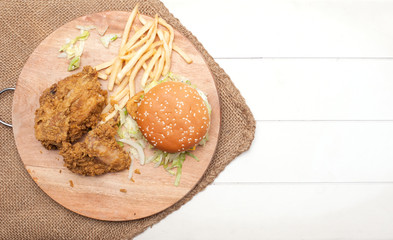 Burger,fries and fried chicken on wooden chopping board isolated over white background.