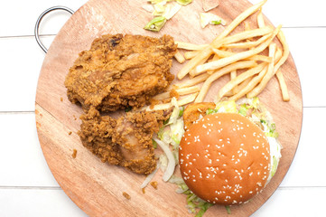 Burger,fries and fried chicken on wooden chopping board isolated over white background.