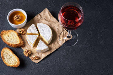 Camembert cheese, toasts, honey, walnuts and glass of wine on a dark background. Flat Lay.