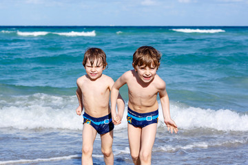 Two kid boys running on ocean beach. Little children having fun