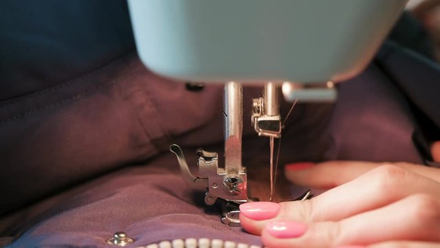 Close-up of seamstresses's hands sews to blue jacket leather inserts on sewing mashine. Side view.