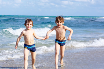Two kid boys running on ocean beach. Little children having fun