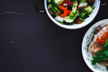Fresh vegetable salad in plate and fish on black background, close up, top view. Healthy food. copy space.