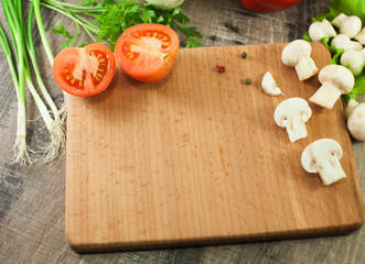 Cutting board and vegetables on wooden background. 