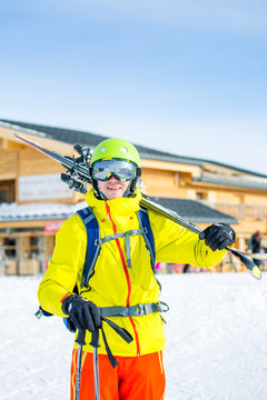 Image of sportive man in helmet with skis on his shoulder against building background