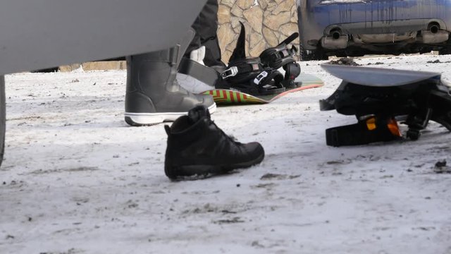 Man puts on shoes for snowboarding near the car on a mountain parking