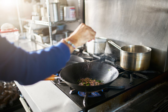 chef in restaurant kitchen seasoning food in hot skillet wok