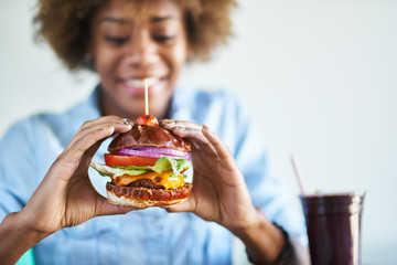 smiling african woman about to eat a meatless vegan cheese burger - obrazy, fototapety, plakaty