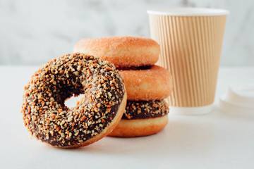 Paper cup of coffee with tasty donuts on white background.