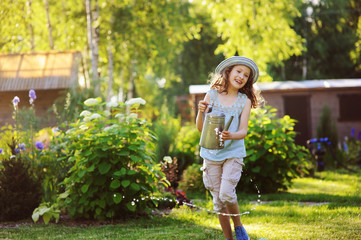 happy funny child girl in gardener hat playing with watering can in sunny summer garden