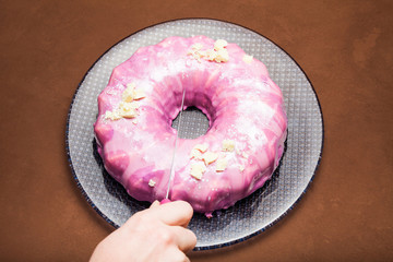 A female hand slices a festive dessert cake on a plate.