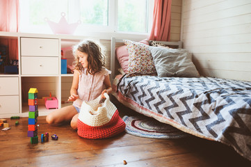 child girl cleaning her room and organize wooden toys into knitted storage bag. Housework and help concept