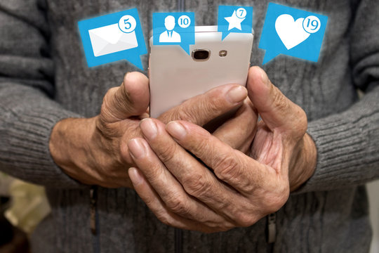 Elderly man holding smartphone with icons of notifications from social media. Social media for the elderly concept. Chat with loved ones in old age.E-learning. - Powered by Adobe