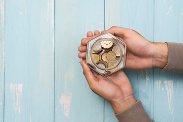 Male hands holding glass jar with coins inside. Top view