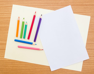 Multicolored crayon pencils lay on grainy white drawing paper over wooden board,top view shot.  