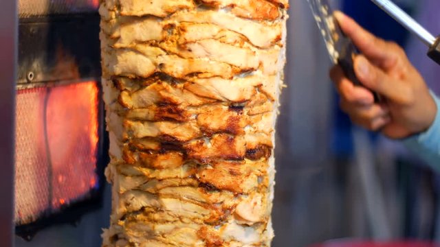 A man with a knife cut meat for shawarma or Denner on a special skewer, close up view. Night market, Pattaya, Jomtien. Thai cuisine. Asian exotic dishes on he market