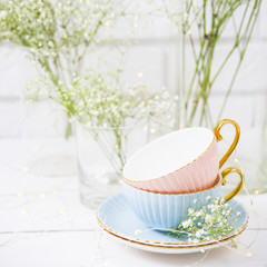 Obraz na płótnie Canvas Delicate vintage cups of pink and blue color among white dry flowers are gypsophila. Home interior concept