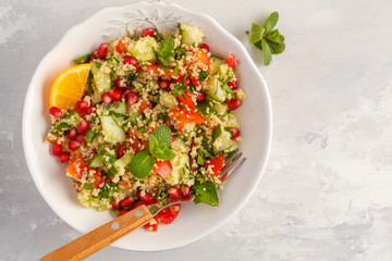 Tabbouleh salad with tomato, cucumber, couscous, mint and pomegranate. Top view, copy space, gray background. Vegan Healthy Food Concept. Traditional middle eastern or arab dish.