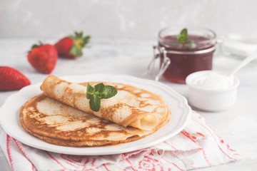 Thin hot pancakes with cottage cheese, jam and strawberries. Healthy traditional breakfast concept.