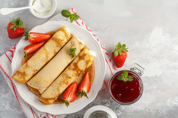 Thin hot pancakes with sour cream, jam and strawberries. Top view, copy space. Healthy traditional breakfast concept.