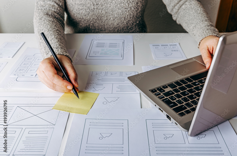 Sticker web designer working at laptop and website wireframe sketches on white table