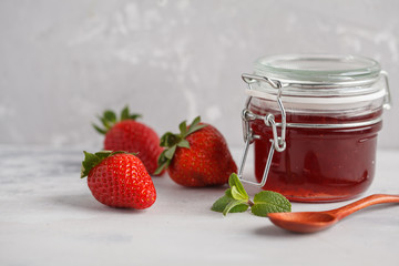 Strawberry jam in a glass jar with berries, gray background.