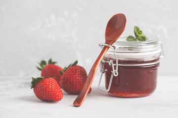 Strawberry jam in a glass jar with berries, gray background.