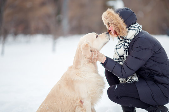 Picture of girl in black jacket embracing labrador in snowy park