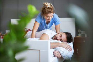 Obraz premium Adorable charming young wife waking up her husband while slipping on the bed. Relationship and weekend goals.