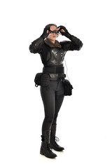 full length portrait of female  soldier wearing black  tactical armour  holding  a pair of binoculars, isolated on white studio background.