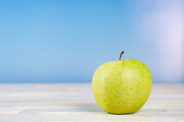 Green apple on wooden table, blue sky background