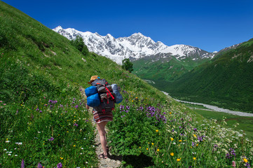 tourist with large backpack rises on mountain trail with view of the Lardaard ice-fall in Georgia...