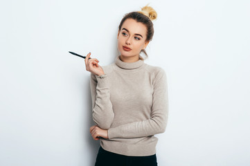 Portrait of Thinking woman with appealing smile, having hair bun in sweater isolated on white...