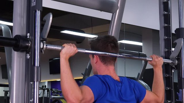 A young fit man does overhead presses in a gym - closeup from behind