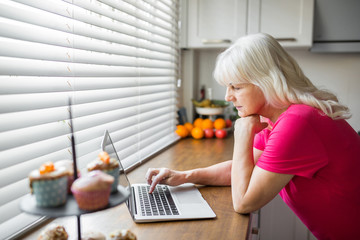 Senior lady using notebook at kitchen