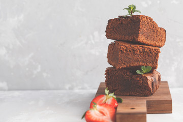 Stack of pieces of homemade dark chocolate brownie with strawberries on a wooden board.
