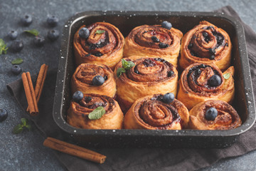 Homemade cinnamon buns with blueberries and cinnamon in oven dish on a dark background