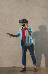 Young man standing in front of wall and using virtual reality headset