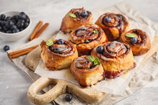 Homemade cinnamon buns with blueberries and cinnamon on a white wooden board