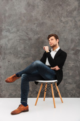 Thoughtful young businessman sitting over grey wall